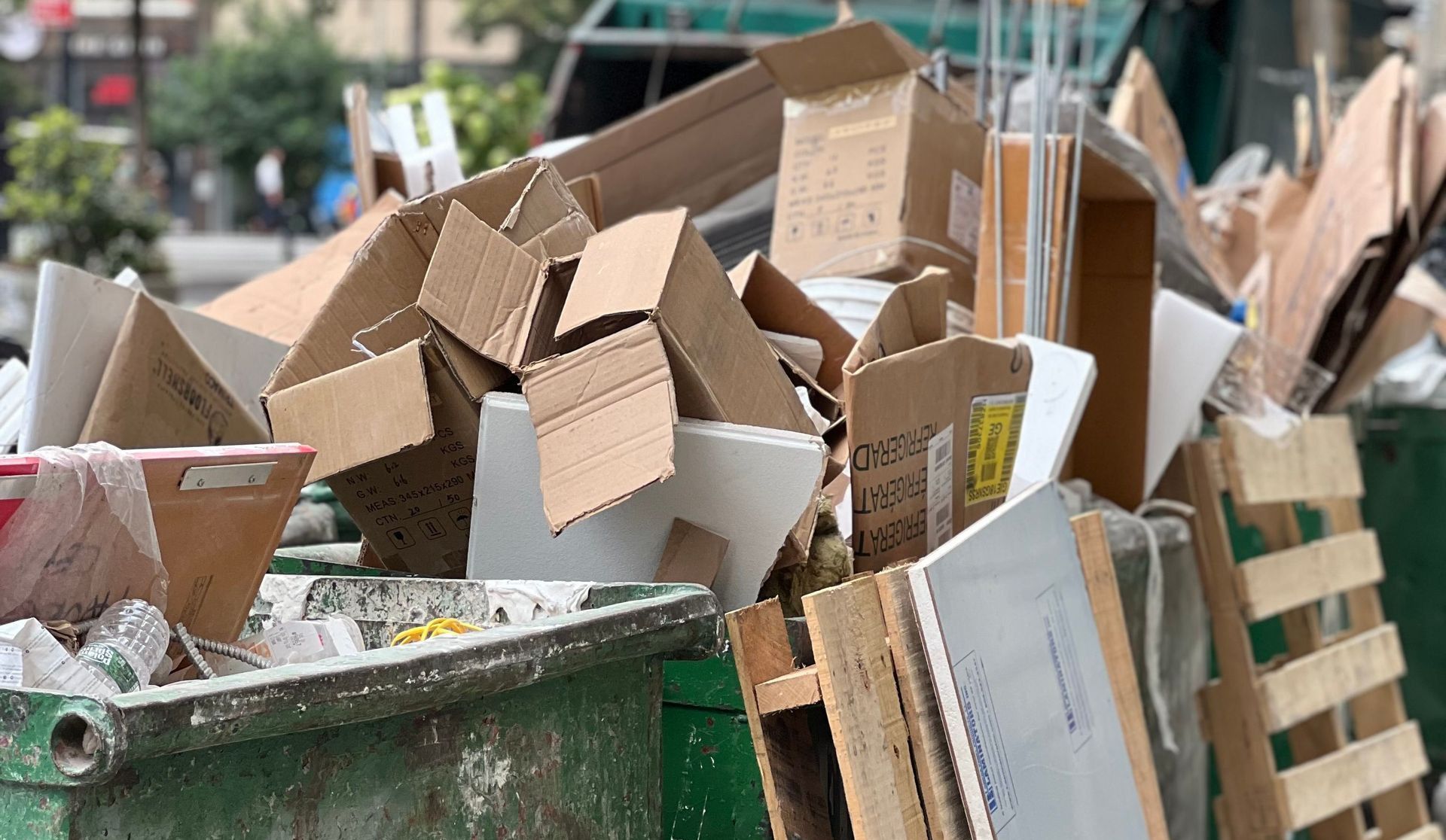 Piled cardboard boxes and waste in a city dumpster highlight urban recycling.